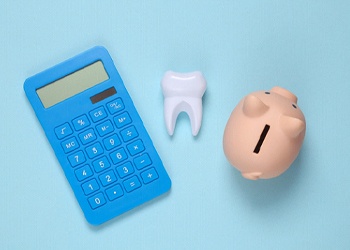 Calculator, tooth, and piggy banked arranged against blue background
