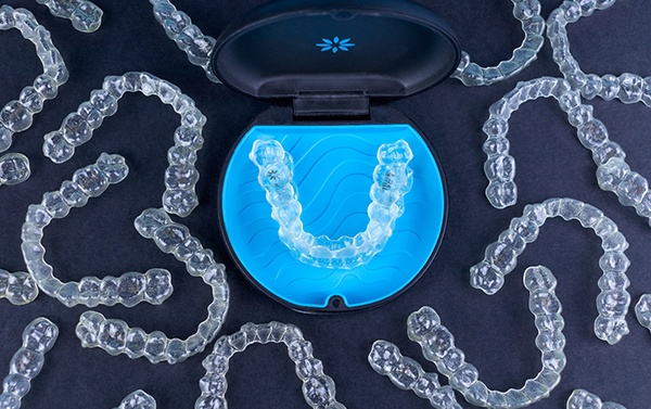 Invisalign aligners in a hard protective case surrounded by dozens of other Invisalign trays that aren’t in cases