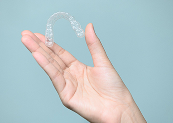 Patient holding Invisalign tray against blue background