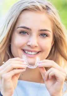 woman smiling while holding Invisalign clear aligner